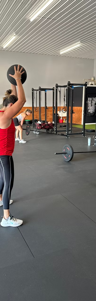 A member lifts a medicine ball overhead during a class at Frontline Fitness 302